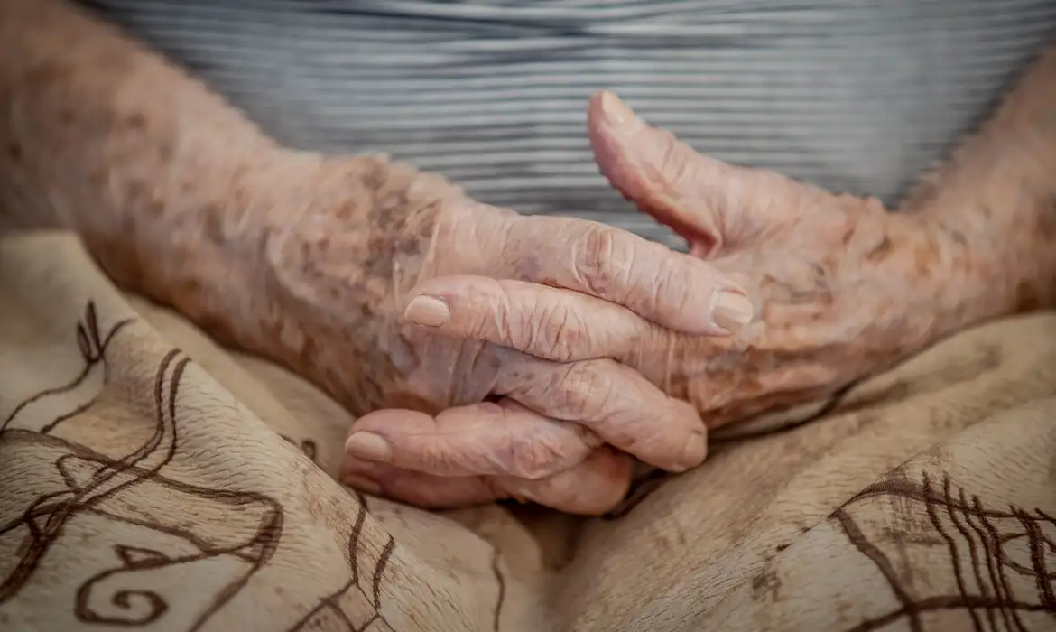 Imagem de uma senhora de idade sentada com os dedos entrelaçados