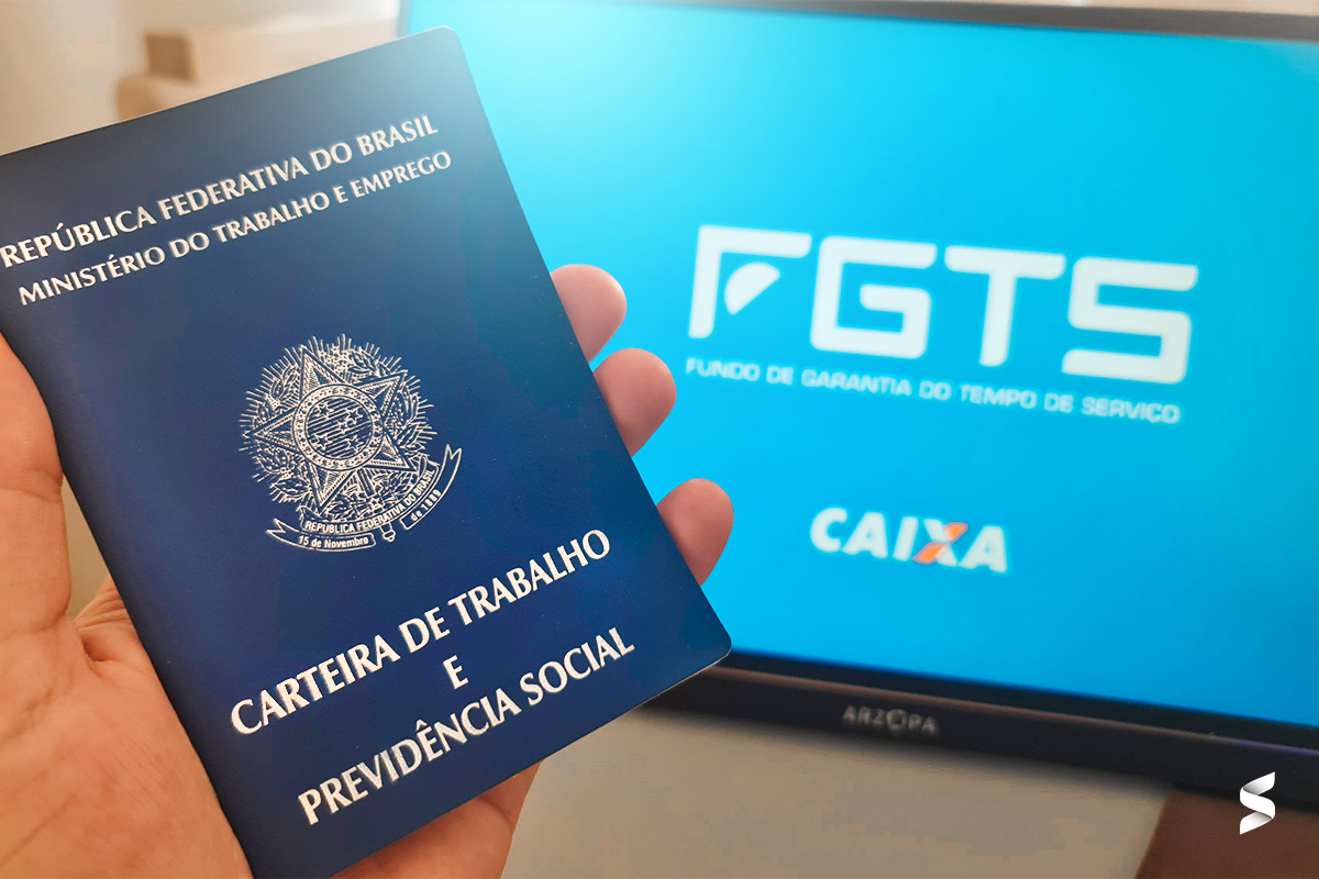 Computador na tela do FGTS com Carteira de Trabalho à frente