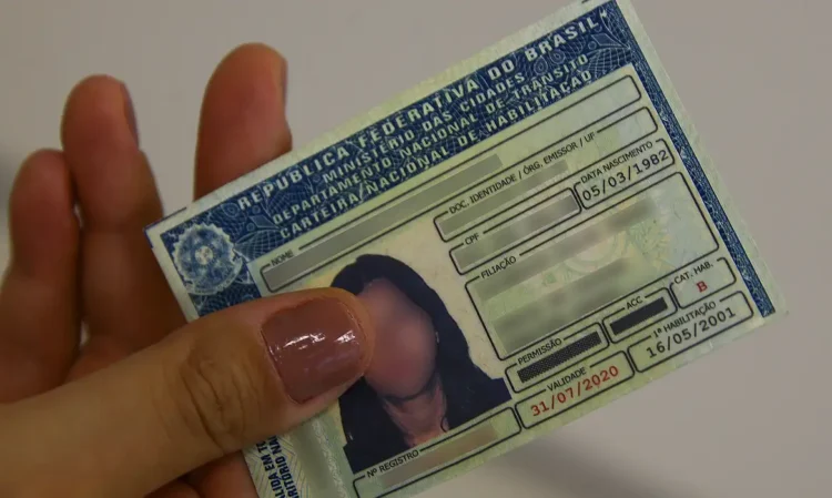 Imagem de uma mão feminina segurando uma CNH.