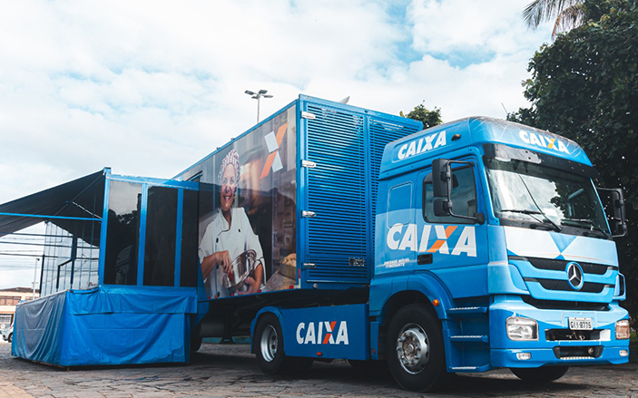 Caminhão da Caixa Econômica Federal adaptado para atendimento móvel, estacionado em área pública.