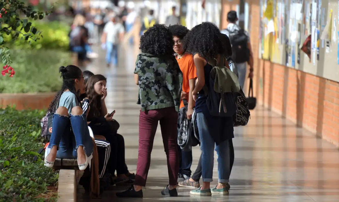 Grupo de estudantes conversando em um corredor universitário, com foco em jovens discutindo oportunidades de financiamento