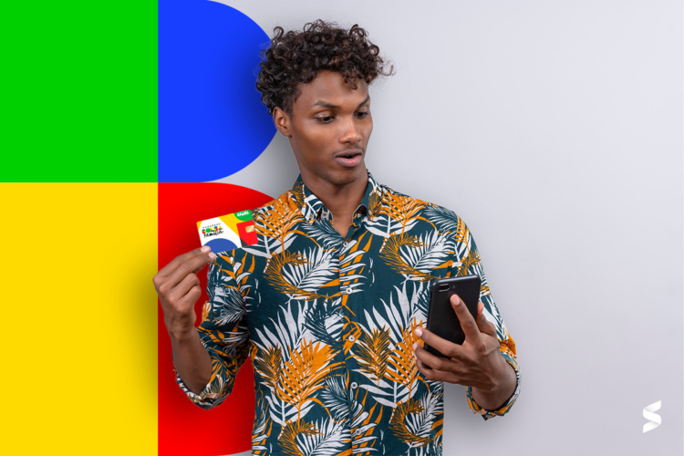 Homem segurando um cartão do Bolsa Família enquanto olha surpreso para o celular.