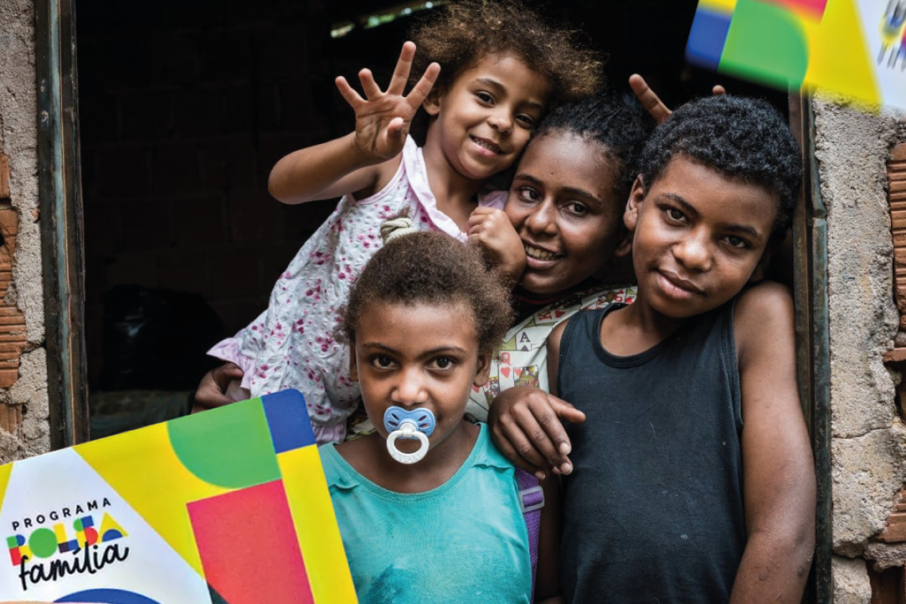 Imagem de um grupo de crianças sorrindo com o cartão do Programa Bolsa Família, em um ambiente simples e alegre, refletindo a importância do apoio social e do auxílio governamental