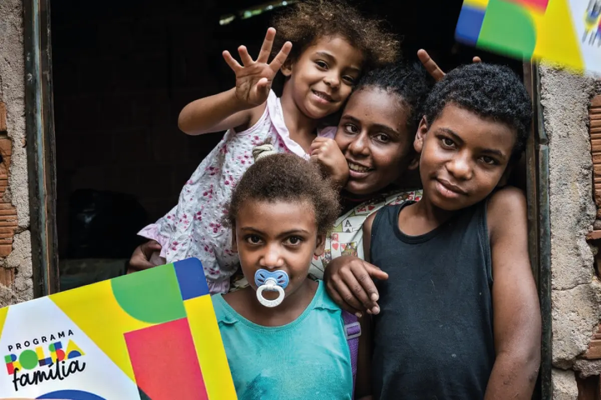 Crianças e adultos sorrindo, com o cartão do Bolsa Família, refletindo a ajuda do programa às famílias carentes.