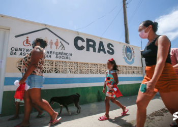 Pessoas caminhando em frente a uma unidade do CRAS, representando o acesso a serviços sociais.