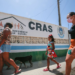 Pessoas caminhando em frente a uma unidade do CRAS, representando o acesso a serviços sociais.