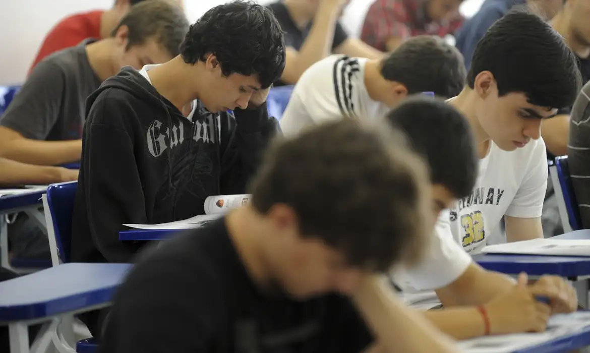 Alunos concentrados escrevendo durante uma atividade em sala de aula.