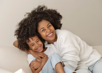 Imagem de uma mãe e seu filho sorrindo, representando afeto e alegria. A mãe está abraçando o filho enquanto ambos estão na mesma posição descontraída e feliz.