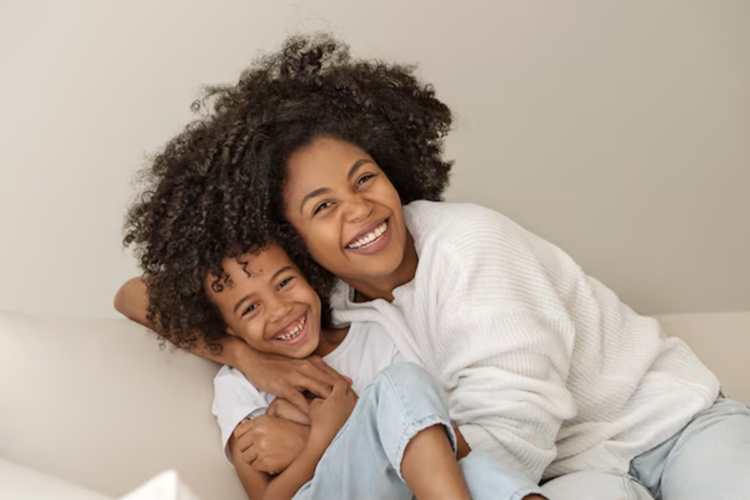 Imagem de uma mãe e seu filho sorrindo, representando afeto e alegria. A mãe está abraçando o filho enquanto ambos estão na mesma posição descontraída e feliz.