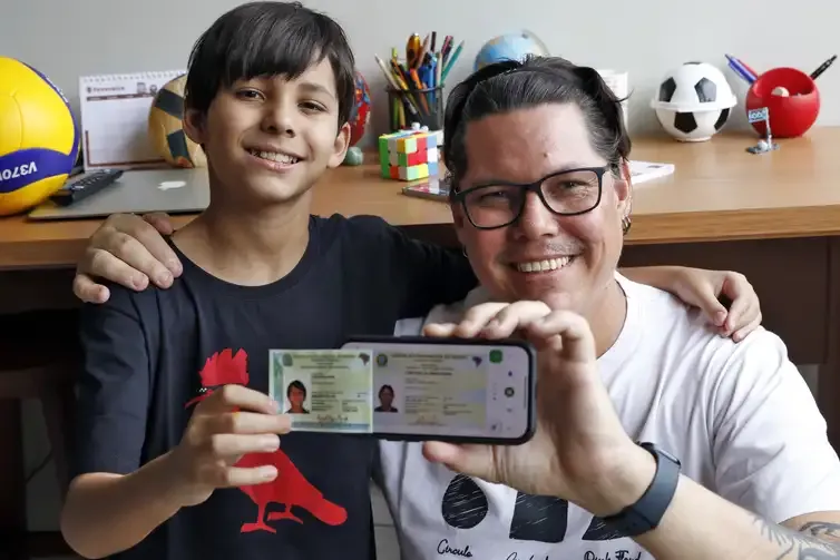 Pai e filho sorrindo e mostrando a nova carteira de identidade no celular.