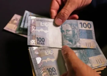 Cédulas de 100 reais sendo contadas, representando o abono salarial que pode ser sacado por trabalhadores