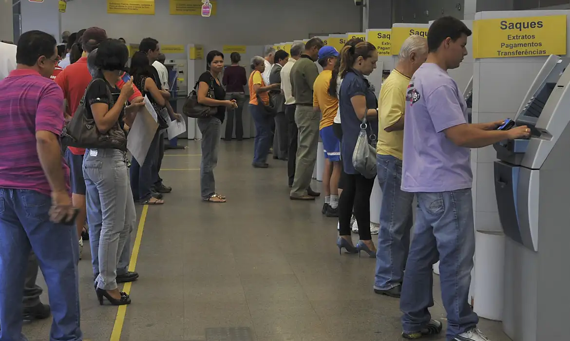 Fila em banco com pessoas utilizando caixas eletrônicos