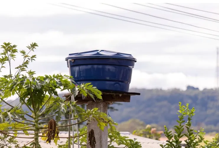 Caixa d'água azul instalada em um poste, com plantas ao redor, como parte de uma ação comunitária.