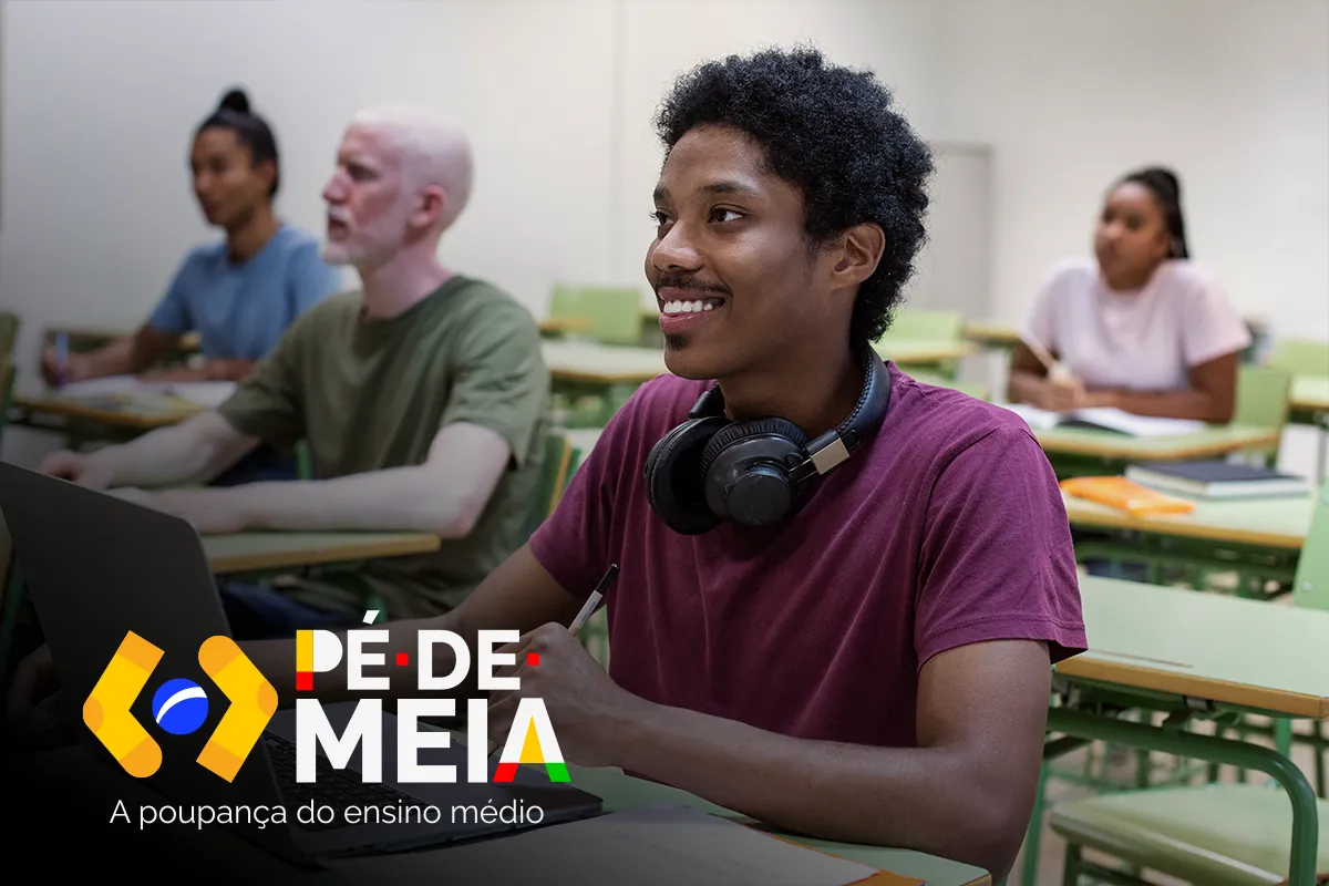 Estudante sorrindo em sala de aula com notebook, representando os beneficiários do programa Pé-de-Meia.