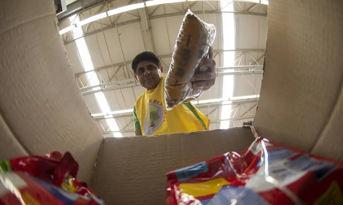 Homem distribuindo pacotes de alimentos de cestas básicas em um local de distribuição.