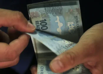 Mãos contando notas de 100 reais, simbolizando o pagamento do INSS.