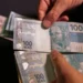 Pessoa segurando notas de R$ 100, representando o pagamento do salário mínimo aos beneficiários do INSS nesta sexta-feira (28).