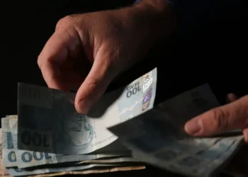 Pessoa segurando notas de R$ 100, simbolizando o valor do salário mínimo a ser pago aos CPFs premiados.