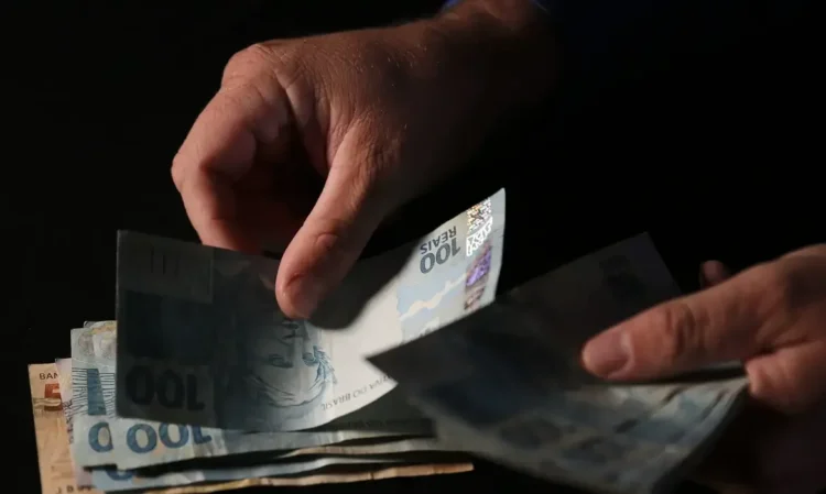 Pessoa segurando notas de R$ 100, simbolizando o valor do salário mínimo a ser pago aos CPFs premiados.
