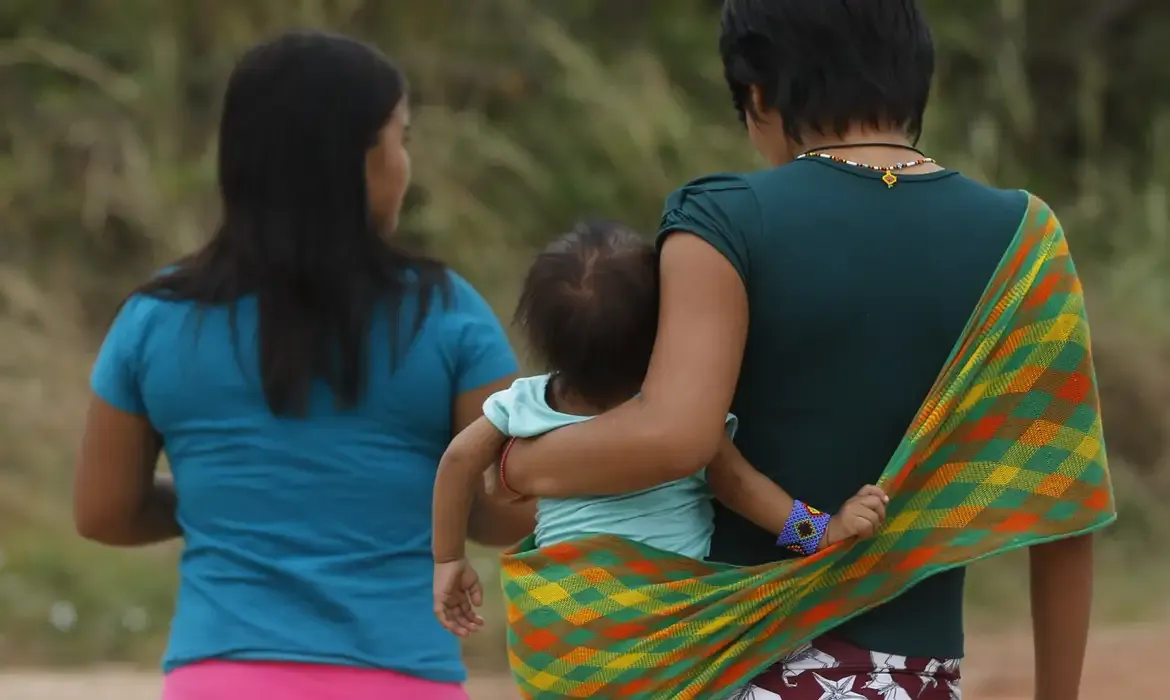 Mulheres indígenas caminhando com uma criança no colo em Uiramutã, Roraima.