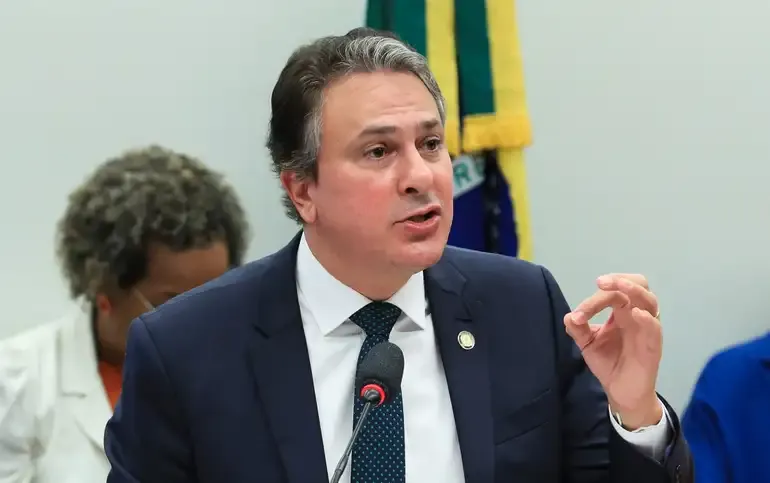 Ministro Camilo Santana falando durante uma reunião, com bandeira ao fundo.