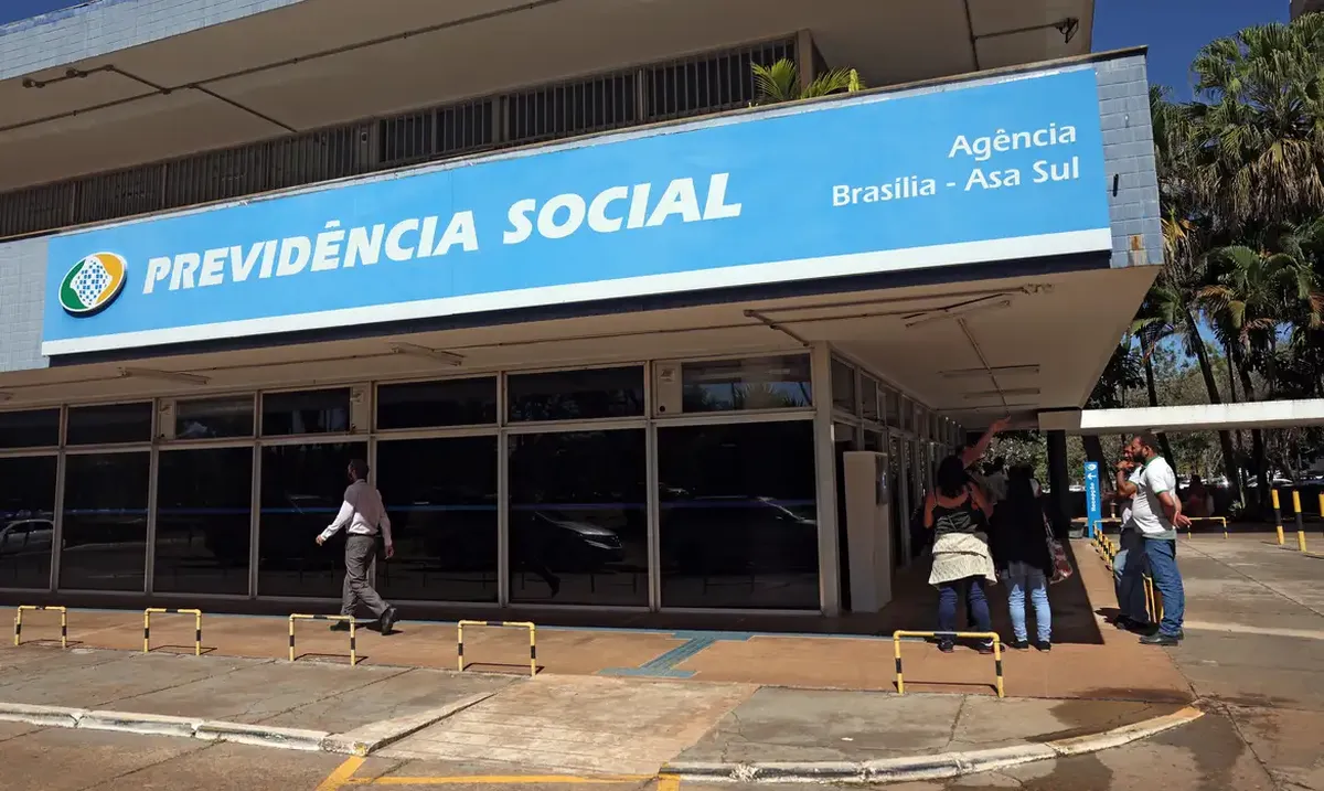 Entrada de agência do INSS com pessoas aguardando atendimento.