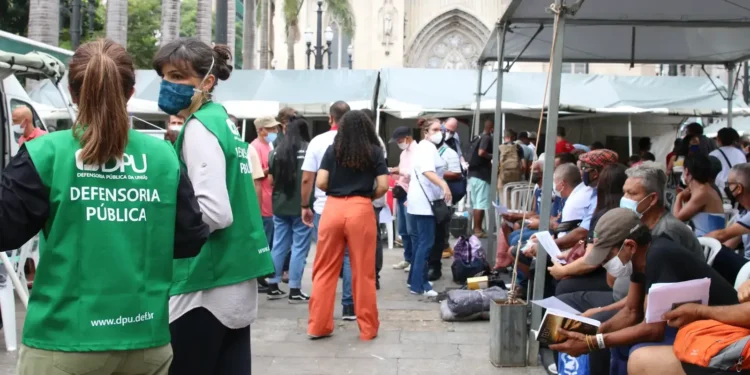 Defensoria Pública e pessoas participando de um mutirão, representando o processo de inscrição para o programa.