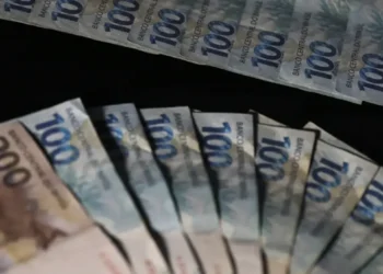 Notas de real espalhadas, incluindo cédulas de R$ 100 e R$ 200, simbolizando auxílio financeiro.