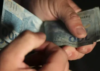 Mãos contando notas de 100 reais, representando pagamentos em dinheiro.