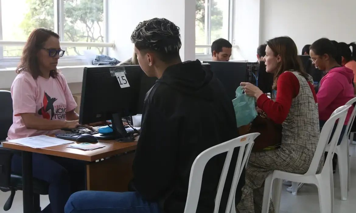 Pessoas em atendimento em uma agência de emprego, ilustrando o processo de inscrição no Programa Bolsa Trabalho.