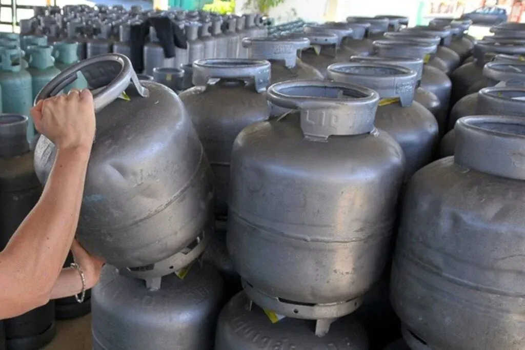 Pilha de botijões de gás com uma pessoa segurando um deles