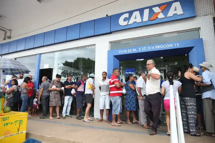 Pessoas fazendo fila em frente à agência da Caixa Econômica para saque do PIS.