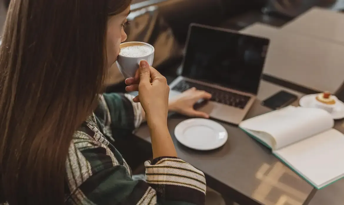 Mulher utilizando um notebook enquanto toma café.