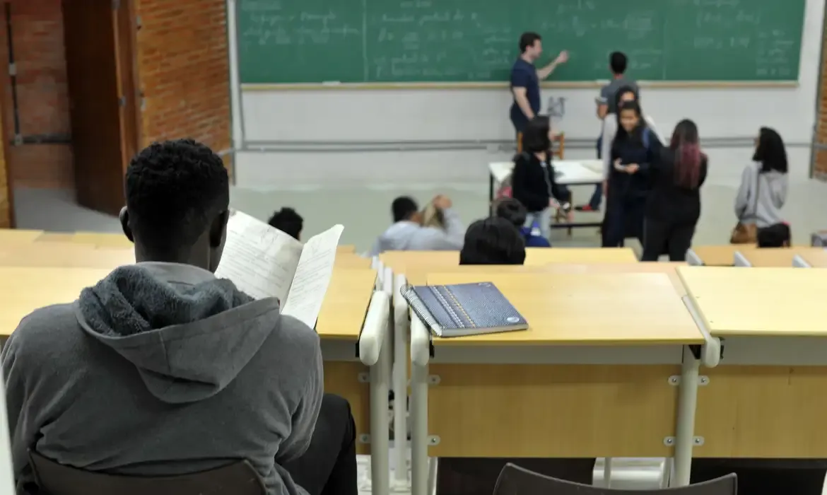 Professor de costas em sala de aula, representando o impacto do programa Mais Professores para o Brasil.