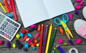 Materiais escolares coloridos sobre mesa rústica, incluindo lápis, tesoura, caderno aberto e calculadora.