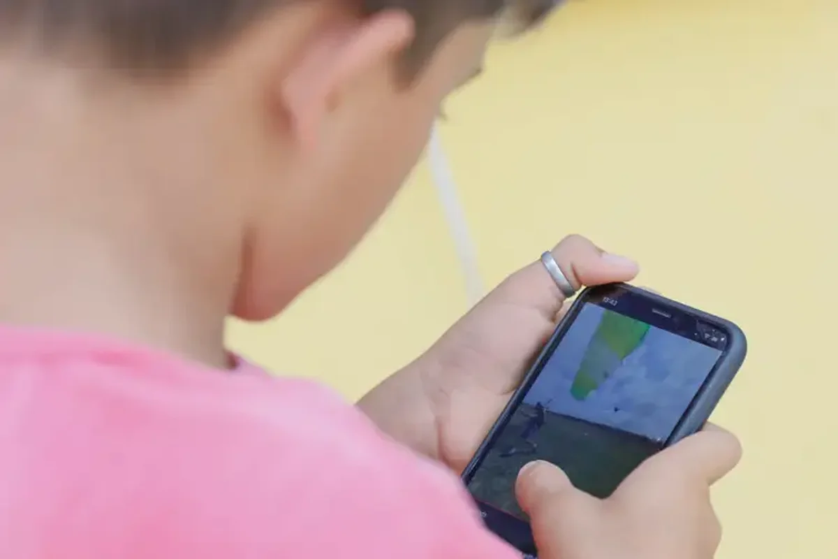 Criança usando um celular no ambiente escolar, refletindo o uso excessivo de dispositivos móveis por estudantes.