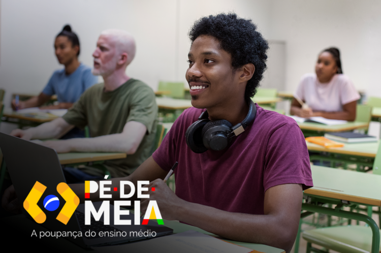 Estudantes em sala de aula com foco no jovem sorrir enquanto usa laptop, representando o pagamento de até R$ 9.200 do programa Pé-de-Meia para estudantes.