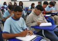 Estudantes concentrados, escrevendo em seus cadernos, durante uma aula em sala de aula.