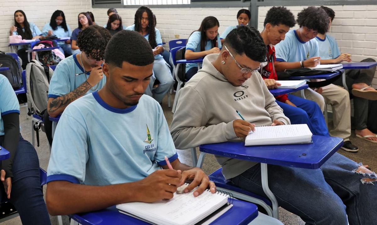 Estudantes concentrados, escrevendo em seus cadernos, durante uma aula em sala de aula.