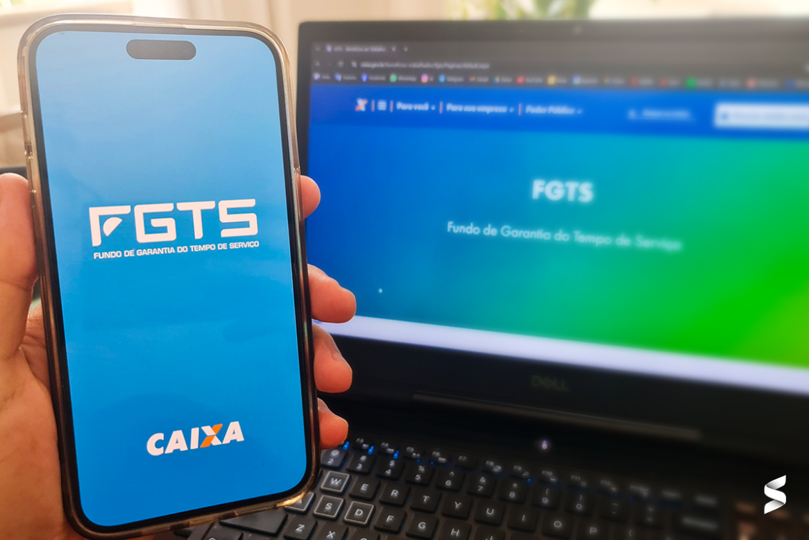 Celular exibindo o logotipo do FGTS com o logotipo da Caixa e site do FGTS aberto em um computador, simbolizando as mudanças no saque-aniversário do FGTS em março.