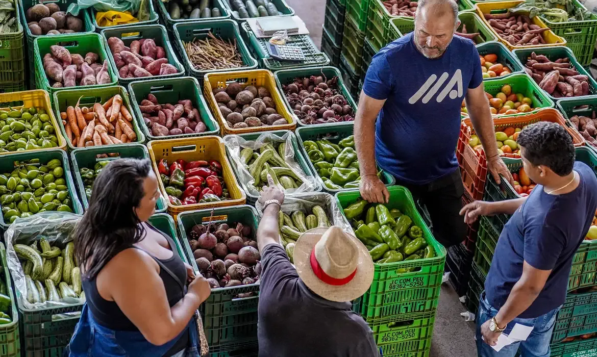 Imagem de um mercado com pessoas comprando alimentos frescos e saudáveis, como vegetais e leguminosas.