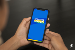 Pessoa segurando celular com a tela exibindo o logo do Cadastro Único, relacionado ao evento 'Cadastro Único Vai Até Você'.