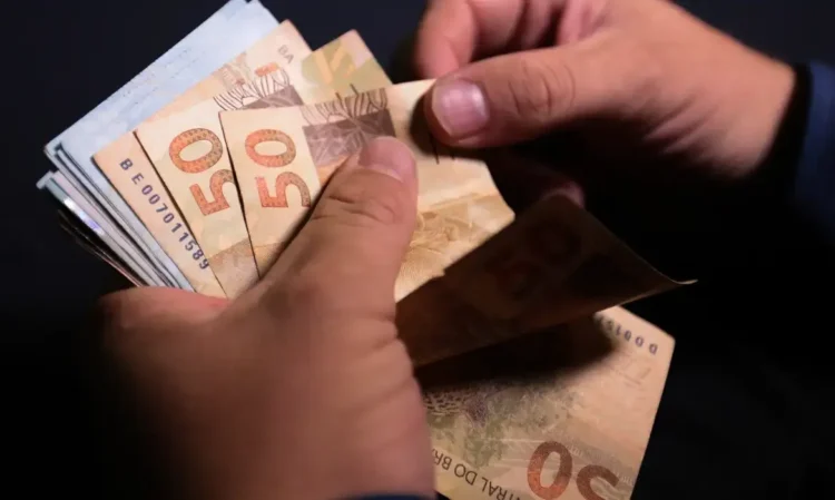 Pessoa manuseando cédulas de dinheiro de 50 reais.