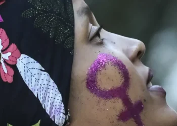 Mulher com símbolo feminino pintado no rosto em glitter roxo.