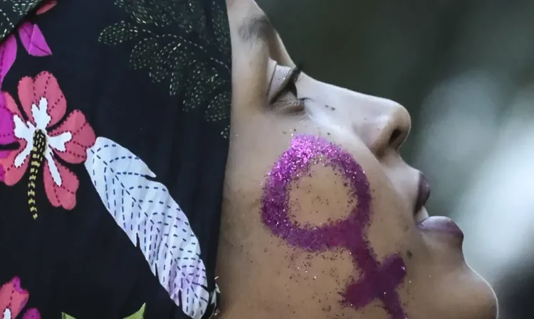 Mulher com símbolo feminino pintado no rosto em glitter roxo.