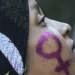 Mulher com símbolo feminino pintado no rosto em glitter roxo.