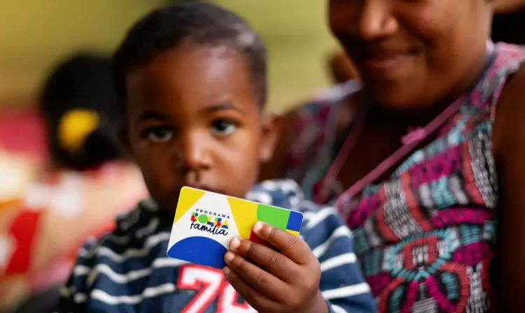 Criança segurando o cartão do Bolsa Família enquanto está ao lado de uma mulher.