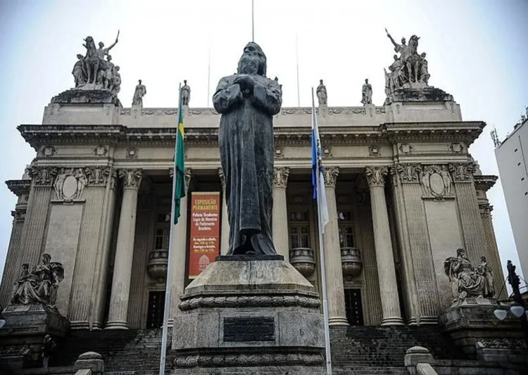 Estátua em frente à Assembleia Legislativa do Rio de Janeiro, com a fachada imponente ao fundo, representando o cenário do feriado de Tiradentes.