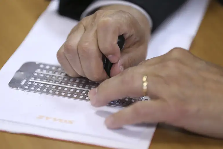 Pessoa utilizando régua e punção para escrever em Braille sobre uma folha.