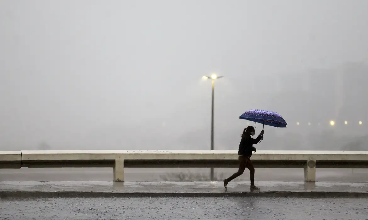 Pessoa caminhando sob chuva, simbolizando o impacto das chuvas na geração de energia hidrelétrica.